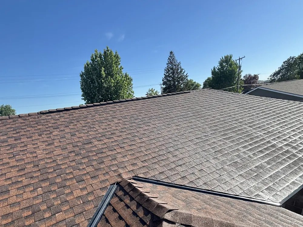 A shingle roof at close range during an inspection, with a second roof plane behind it
