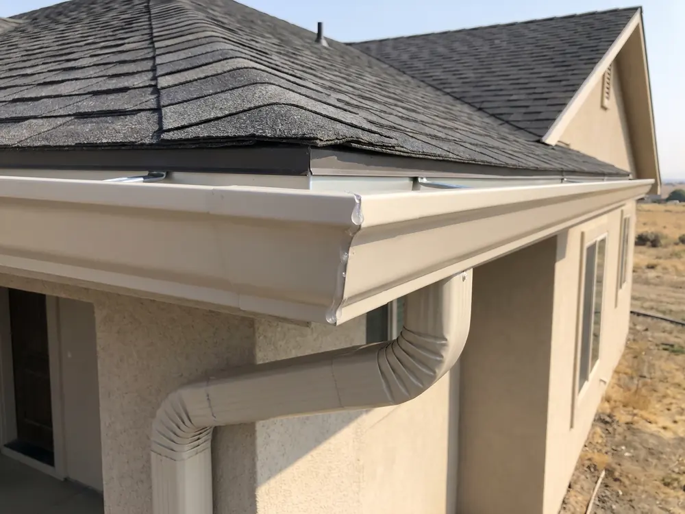 A close view of a new seamless gutter where the downspout outlet meets the corner