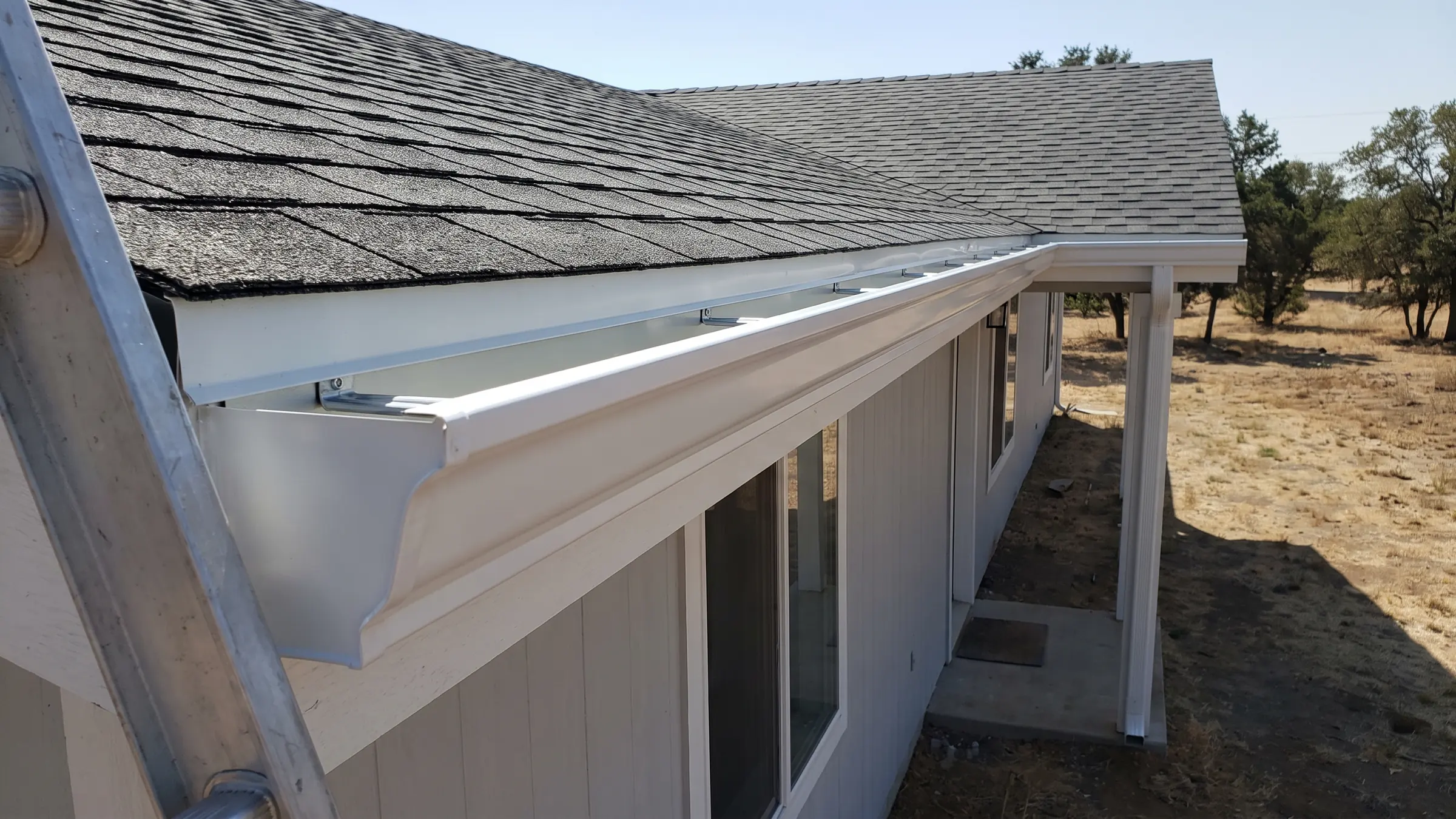 A run of newly installed seamless gutter along the fascia, with the roof edge above and a downspout at the corner