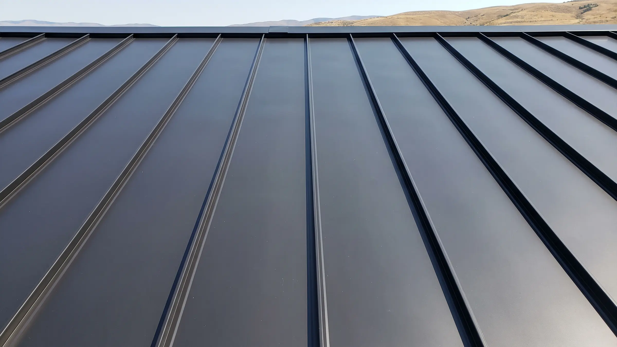 A new dark charcoal standing seam metal roof, the raised seams running toward the ridge
