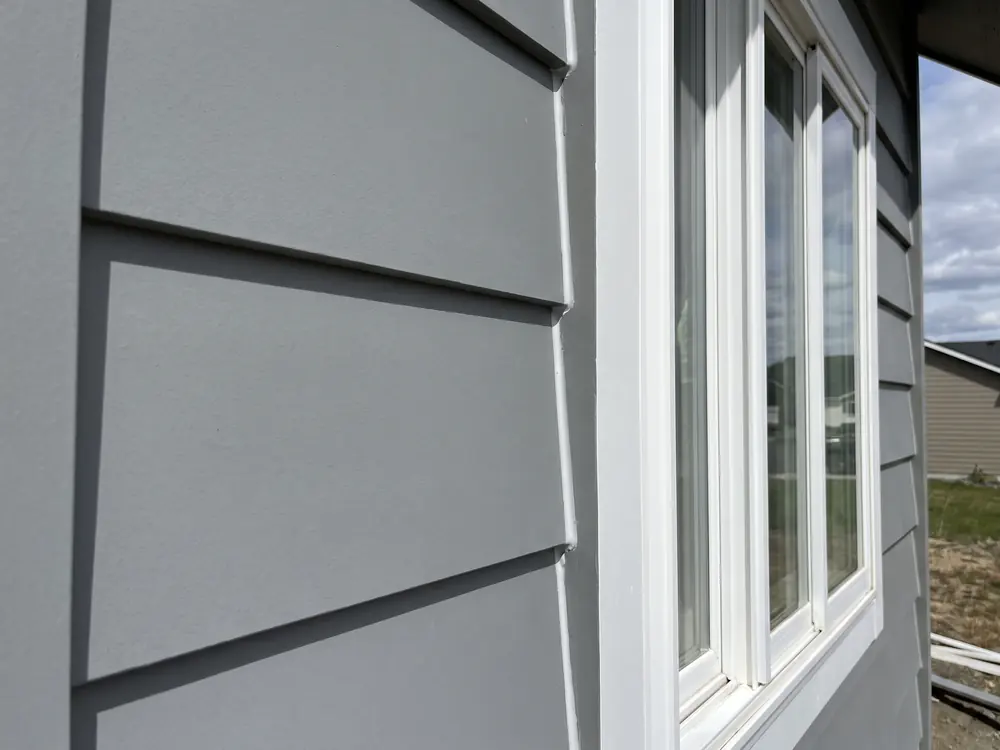 A close view of new fiber cement lap siding and white trim beside a window