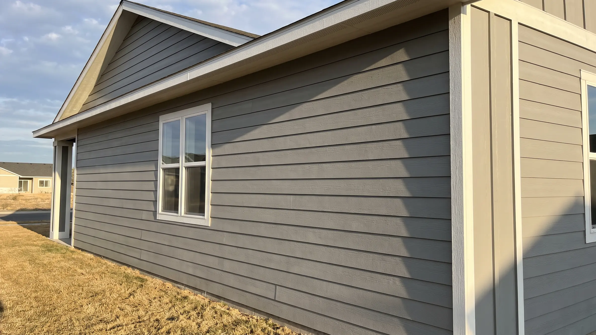 Newly installed grey fiber cement lap siding meeting white corner trim on a home exterior