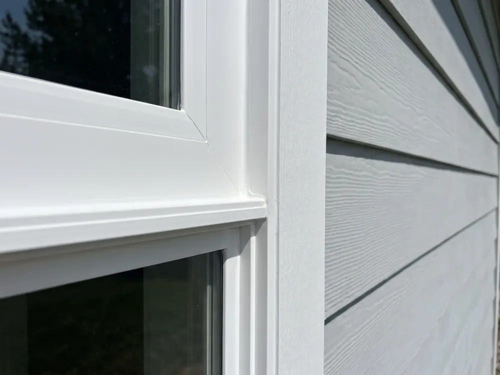 A close view of the corner of a new white window frame meeting exterior trim and siding