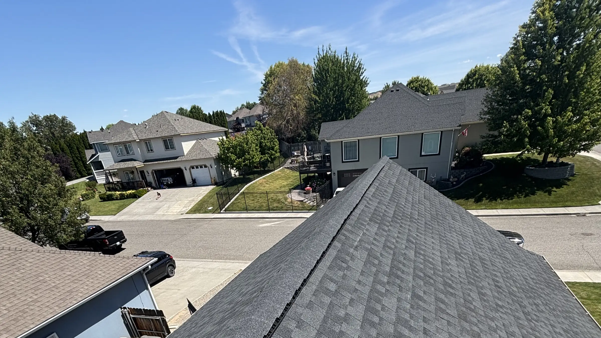 A finished shingle roof with a street of Eastern Washington homes and mature trees behind it
