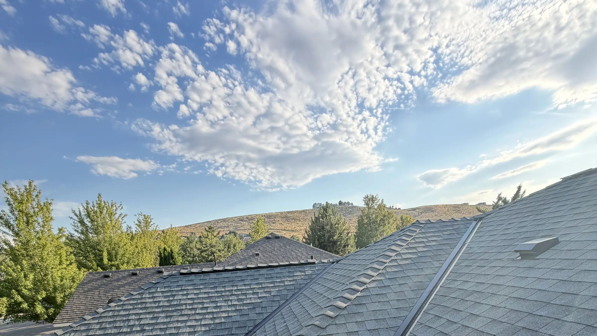 A finished shingle roof with an Eastern Washington hillside and a bank of cloud behind it
