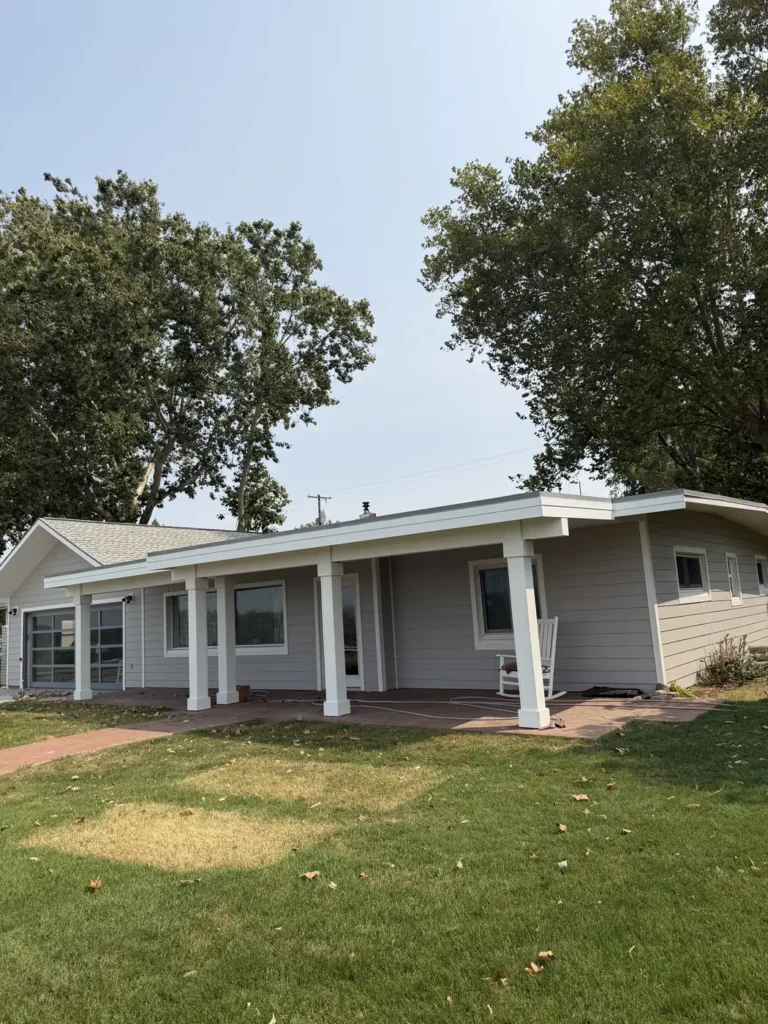 A completed home exterior seen from the front lawn, with a covered porch and mature trees