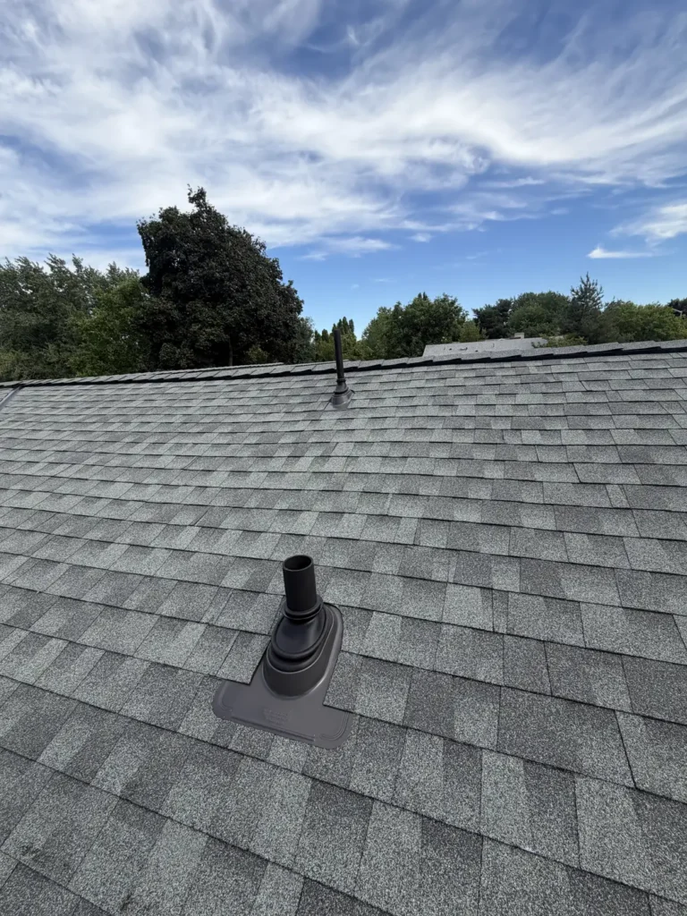 A pipe vent set into new shingle, under a cloud bank