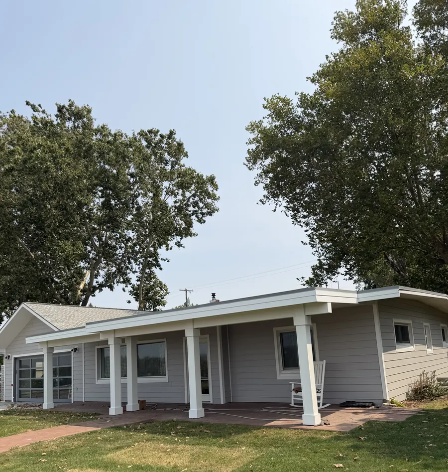 A completed home exterior seen from the front lawn, with a covered porch and mature trees