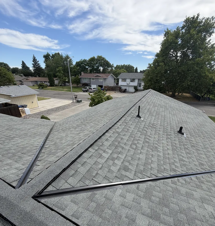A completed shingle roof seen from the ridge, with the street and neighbouring homes beyond